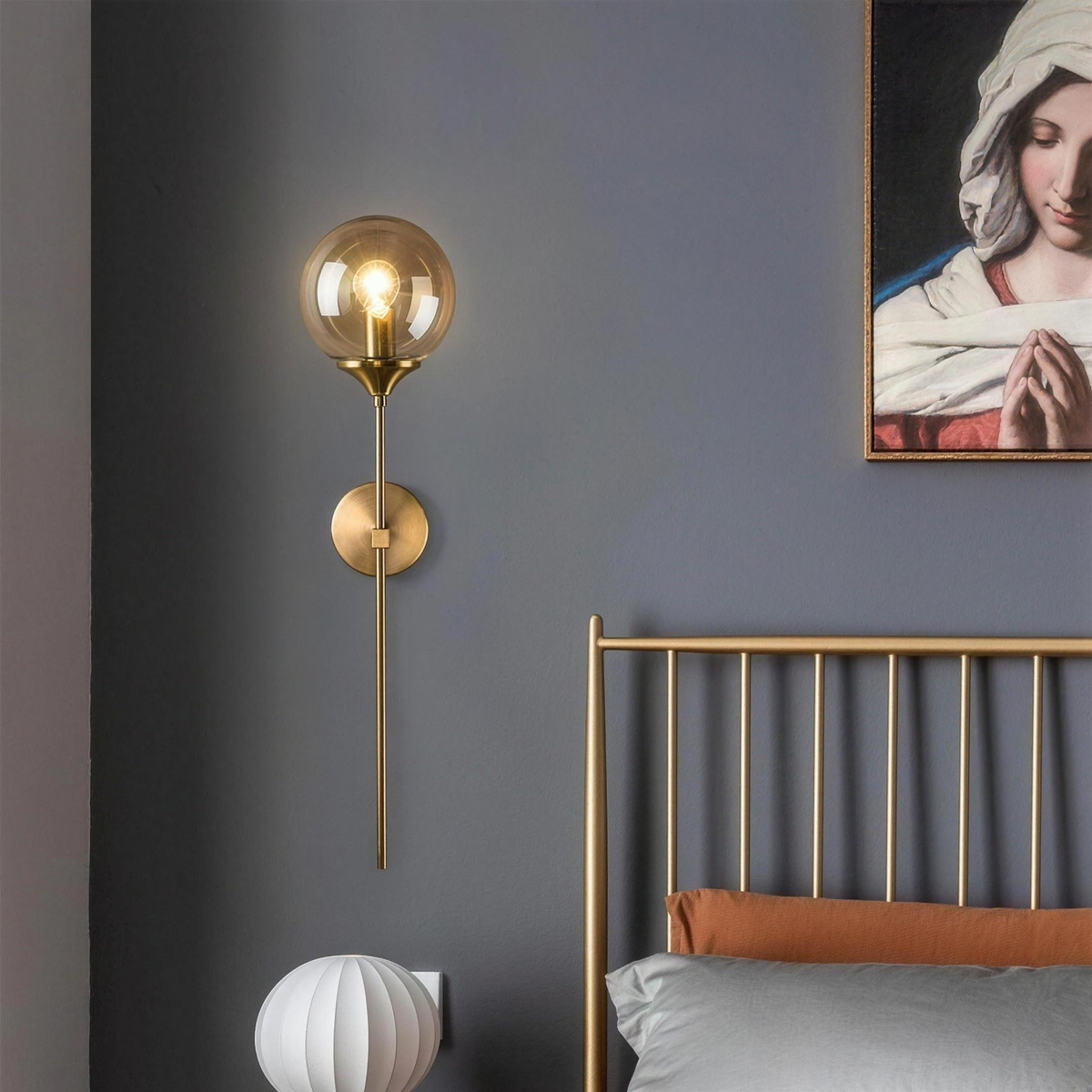 Marlow gold wall light with clear globe beside a brass bed - Hestia + Co.