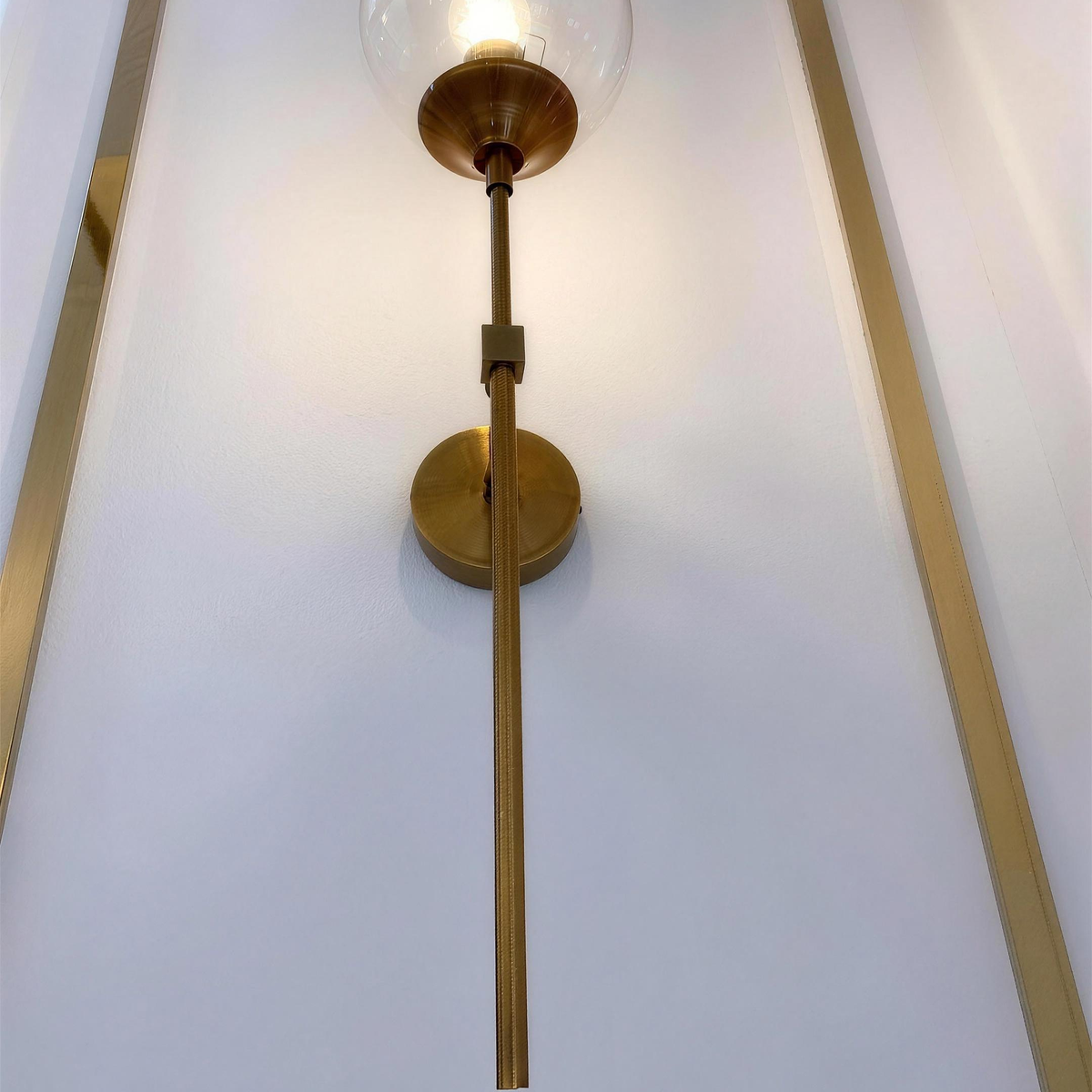 Marlow gold wall light switched on against panelled wall - Hestia + Co.