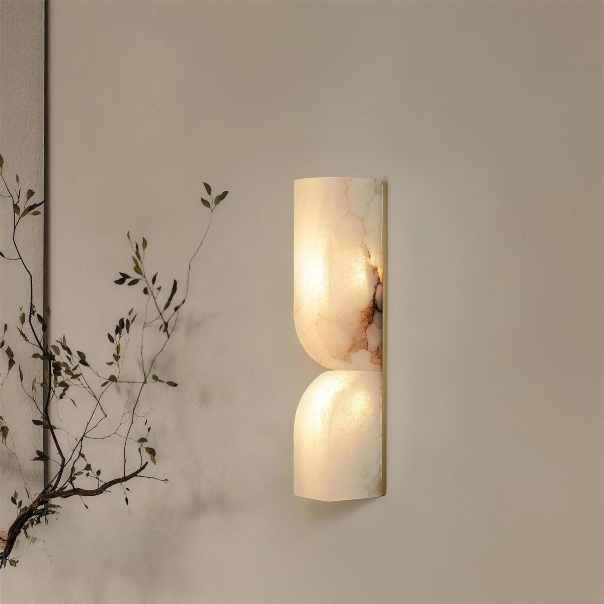 Ronda marble wall light lit on a beige wall with a dried branch - Hestia + Co.