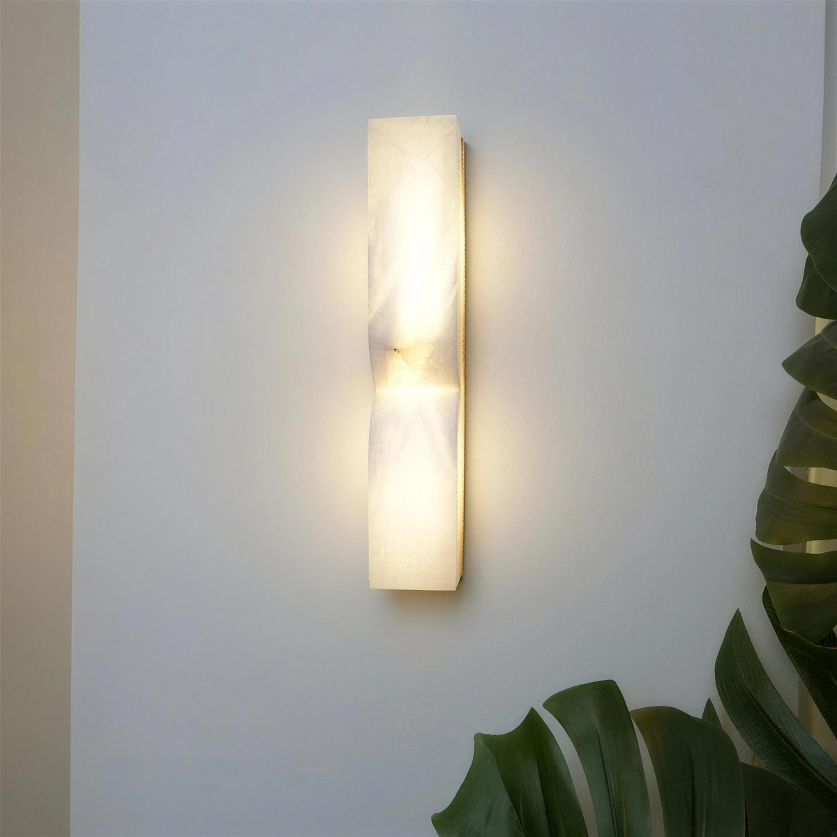 Ronda marble wall light lit on a white wall beside a monstera - Hestia + Co.