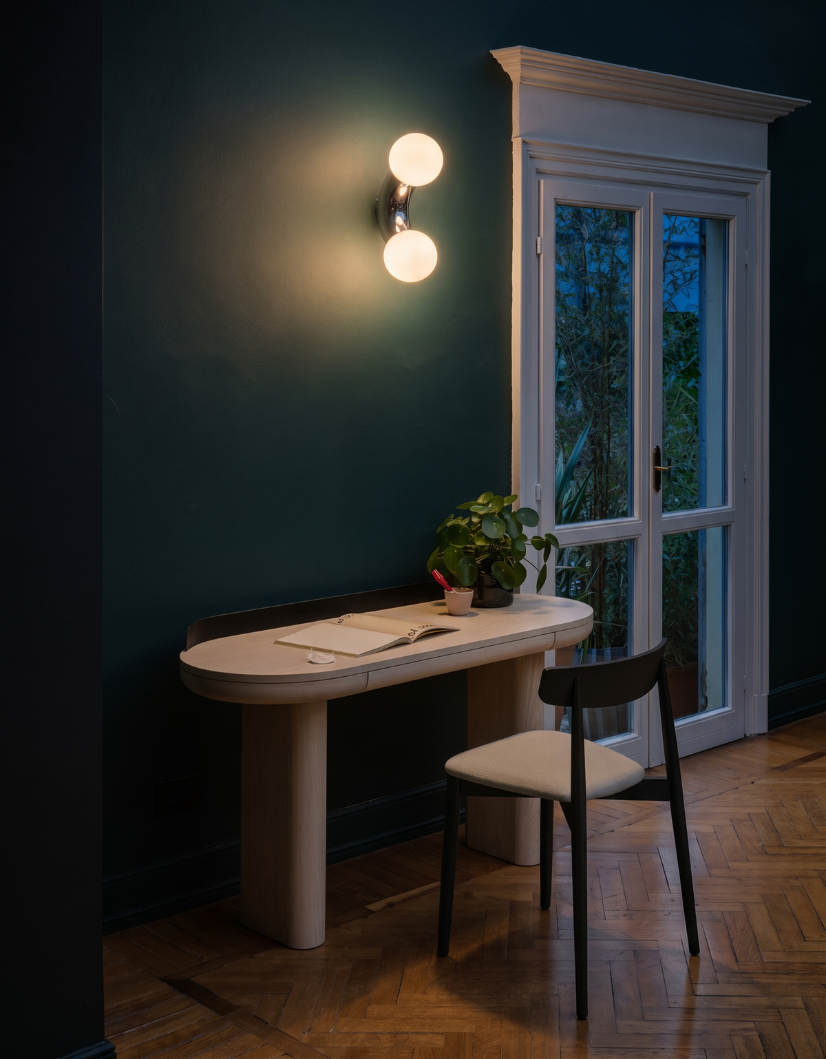 Como wall light glowing at night above a desk on a teal wall - Hestia + Co.