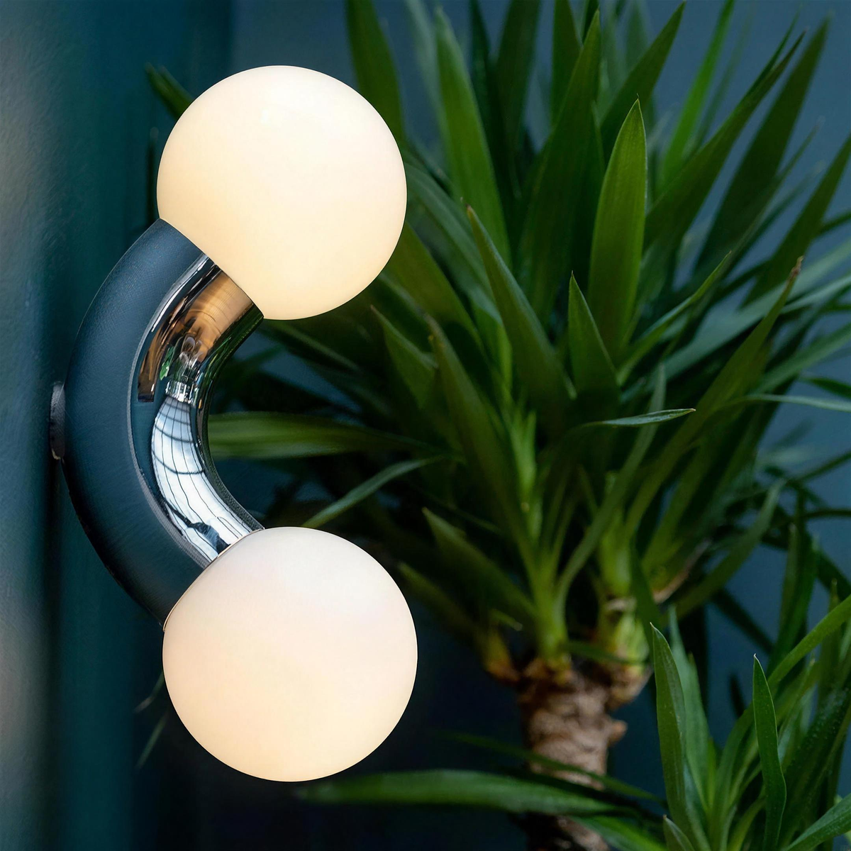 Como wall light close up, chrome arc and frosted glass globes against a teal wall - Hestia + Co.