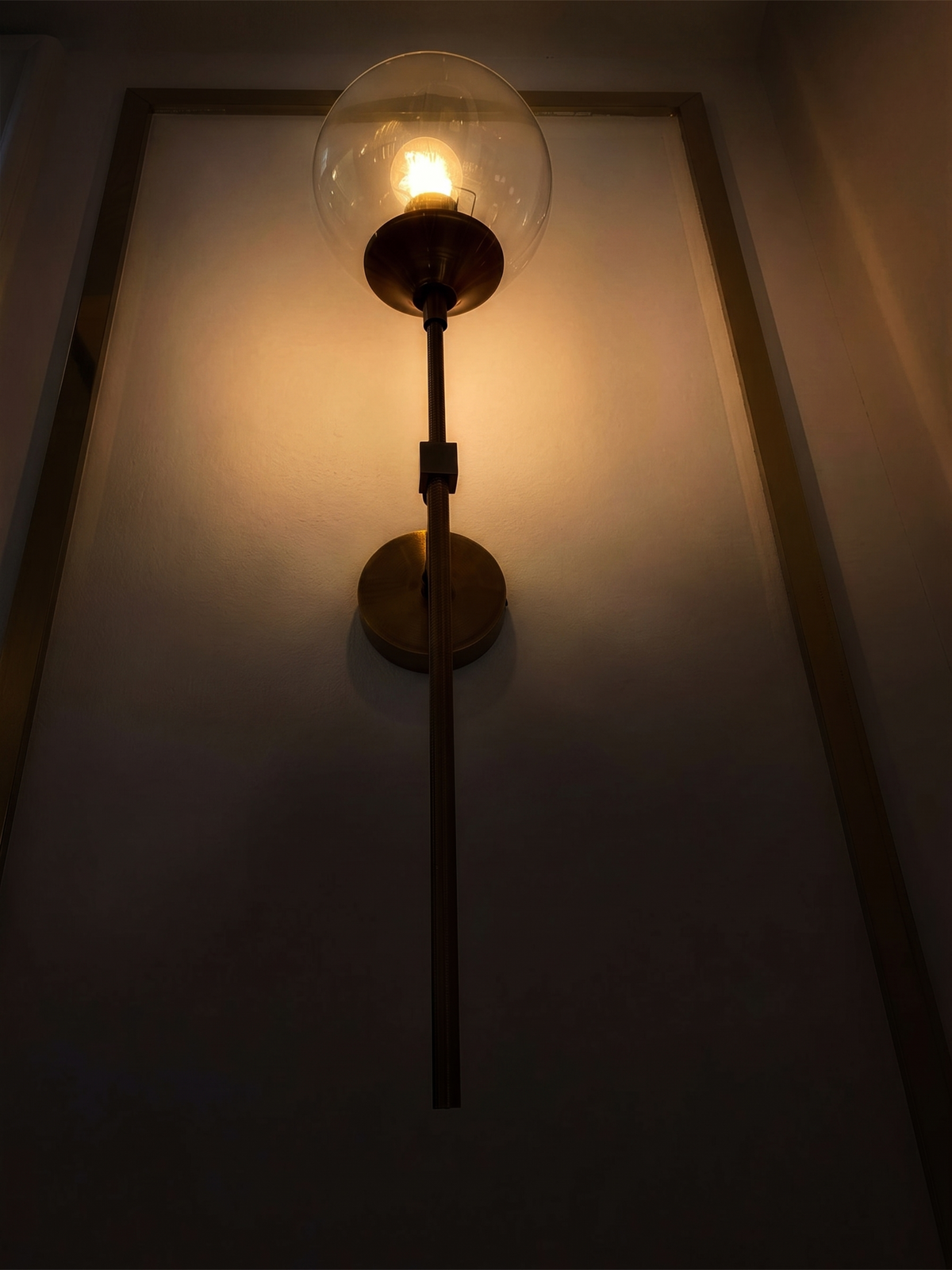 Marlow gold wall light glowing at night against a panelled wall - Hestia + Co.