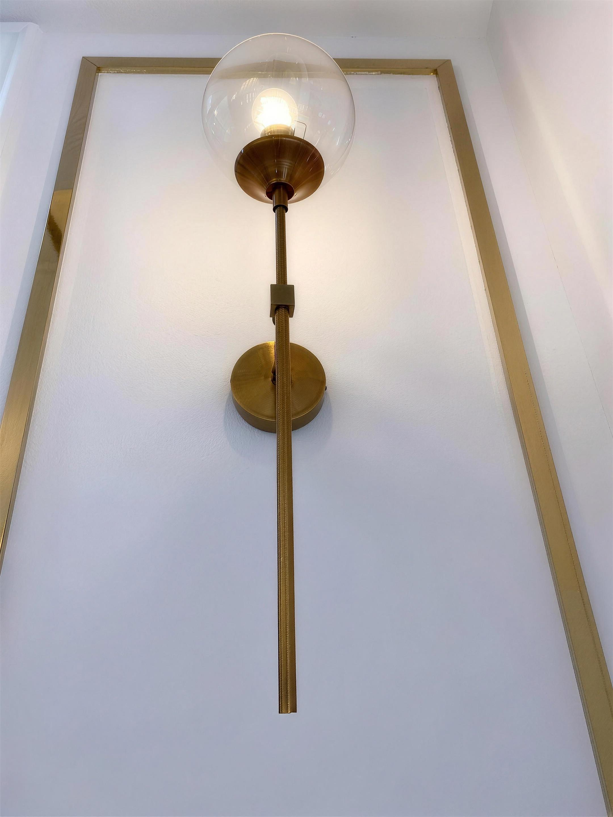 Marlow gold wall light switched on against panelled wall - Hestia + Co.